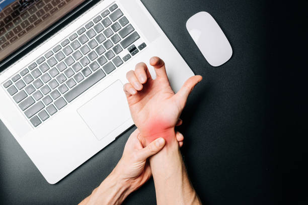 Person holding a painful, red wrist from carpal tunnel syndrome while working at a laptop, illustrating repetitive strain and the need for non-invasive treatment.