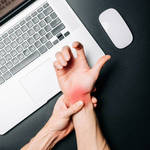 Person holding a painful, red wrist from carpal tunnel syndrome while working at a laptop, illustrating repetitive strain and the need for non-invasive treatment.