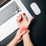 Person holding a painful, red wrist from carpal tunnel syndrome while working at a laptop, illustrating repetitive strain and the need for non-invasive treatment.